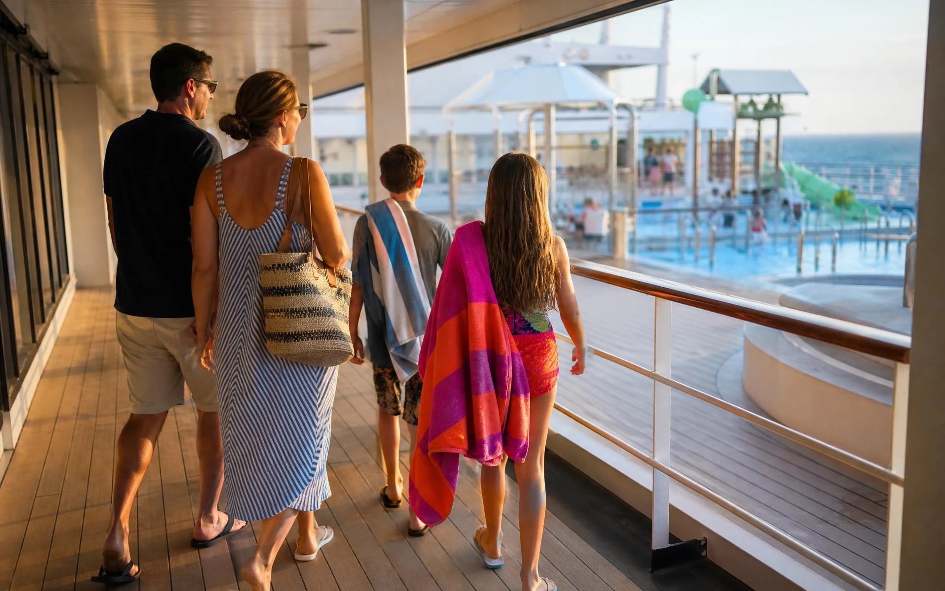 A family of four walking from their cabin deck toward the ship's pool area in late-afternoon light